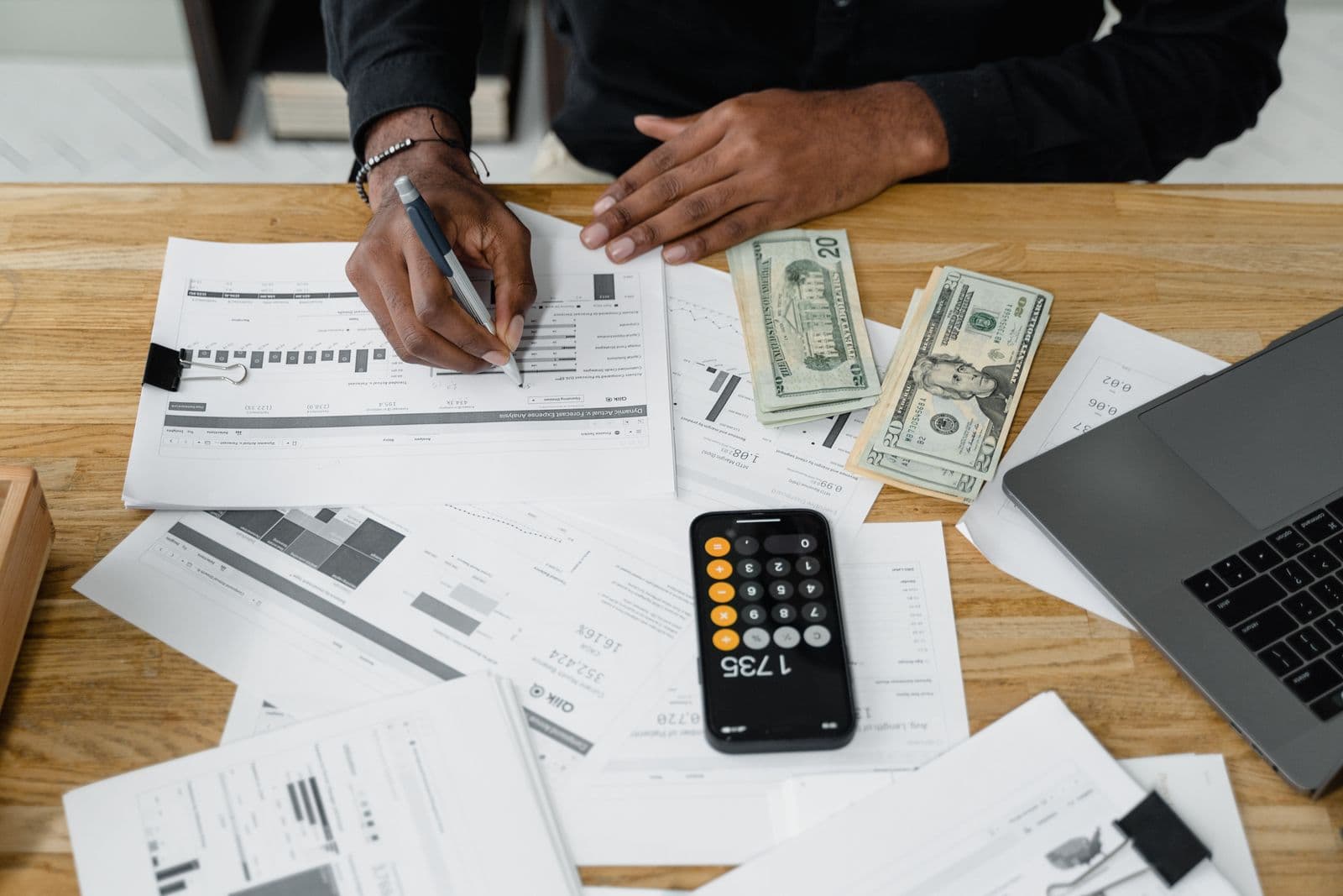 A hand marking up a printed financial report on a wooden desk